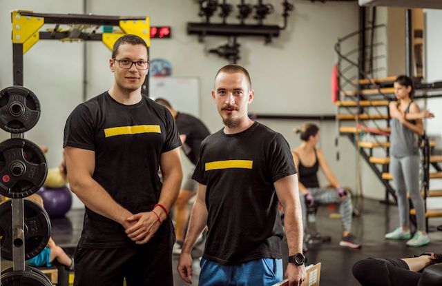 Two white men who small business owners, standing at their local gym and asking if gym memberships are tax deductible.