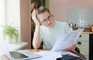 woman holding a pencil wearing glasses looking over a document at her desk looking confused